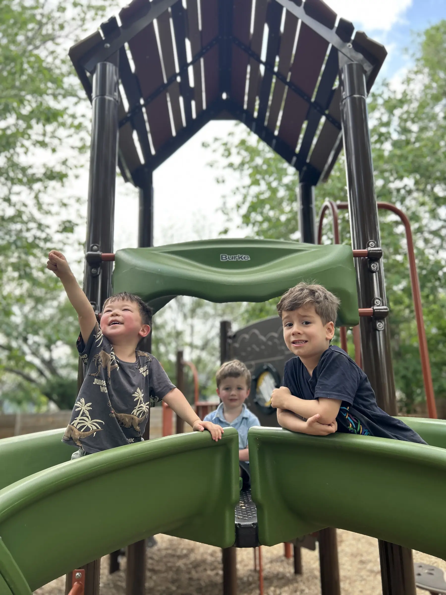 Three Mockingbird preschoolers playing together on the shaded playscape
