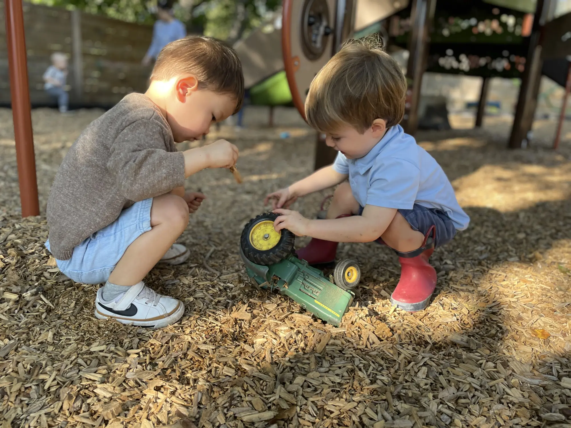 Two Mockingbird toddlers working together with a toy tractor on the playscape
