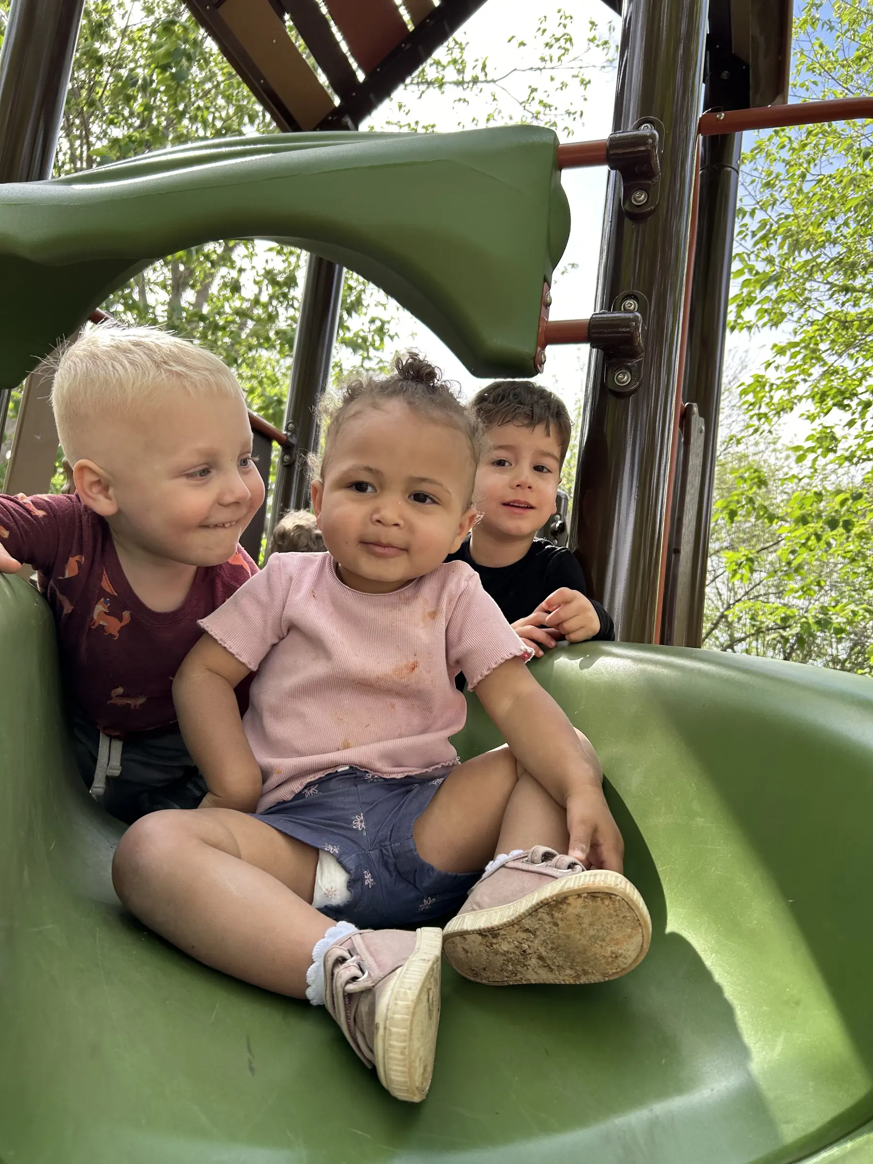 Three Mockingbird toddlers sitting together at the top of the playscape slide